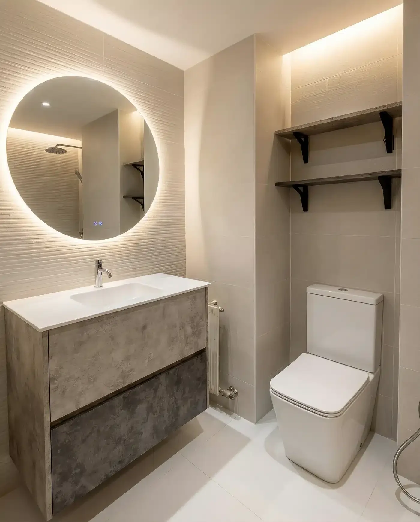 Baño terminado con mueble suspendido de dos cajones, lavabo blanco, espejo circular retroiluminado y estantes sobre el inodoro.